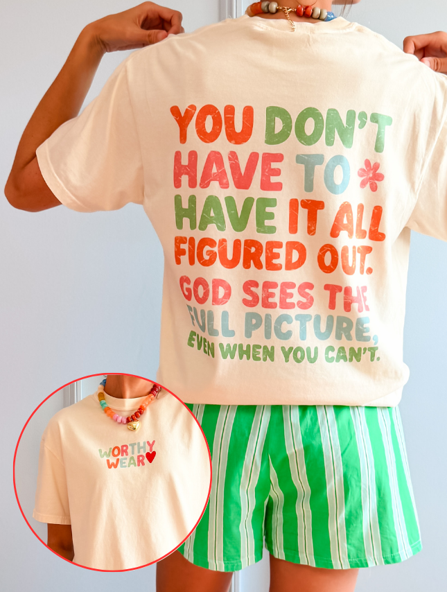 God Sees Front + Back Tee in cream with colorful text on back and small "Worthy Wear" logo on front.