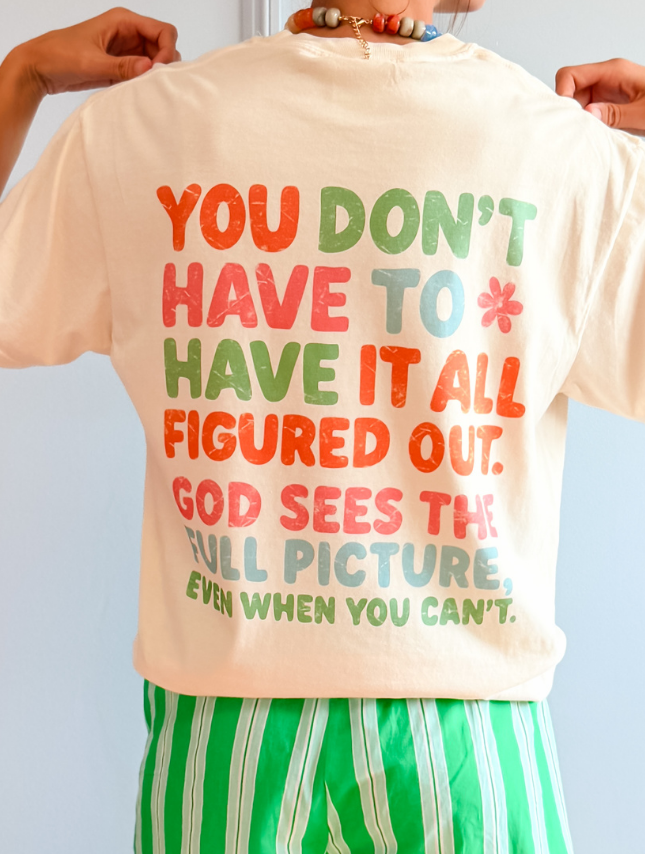 Cream-colored tee featuring colorful text on the back: "You don't have to have it all figured out. God sees the full picture.