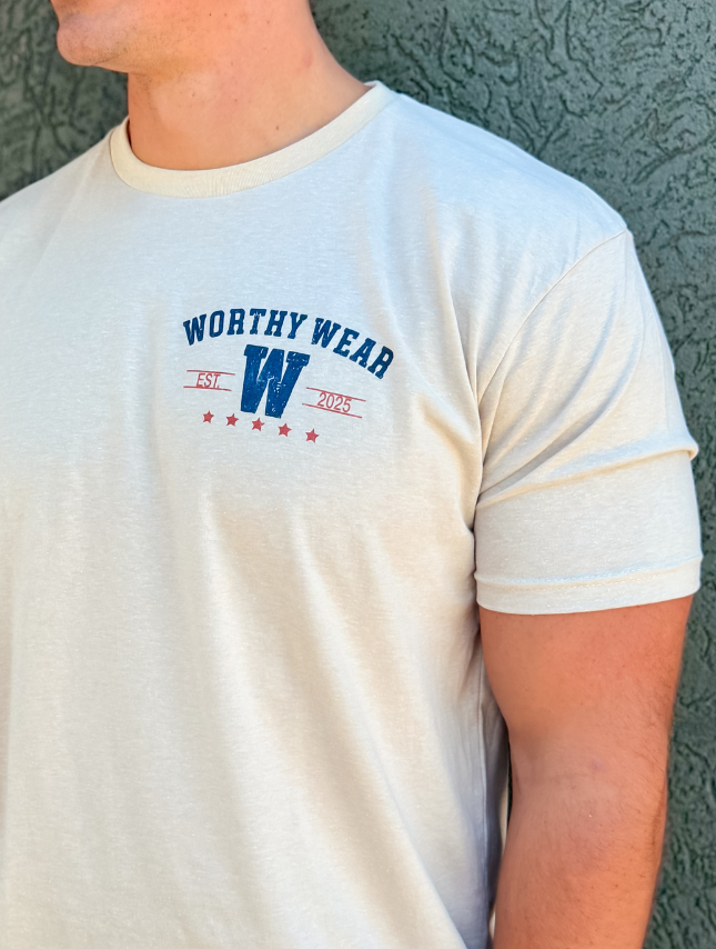 Cream-colored vintage Goodness tee featuring a blue and red graphic with "Worthy Wear" and stars on the chest.