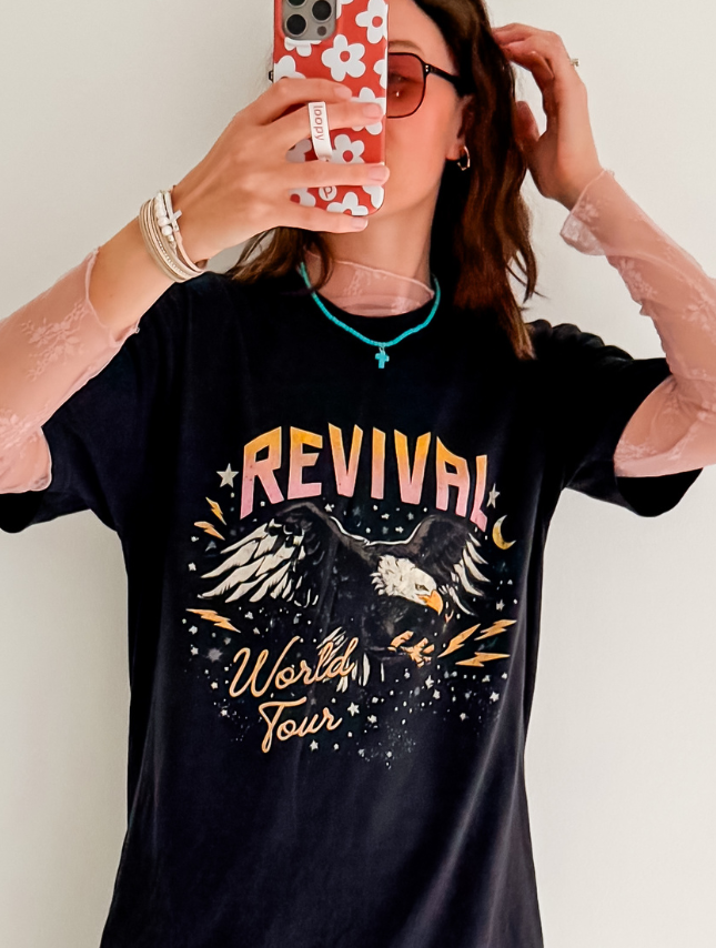 Revival World Tour tee featuring an eagle graphic, black fabric, and colorful design elements worn by a person.