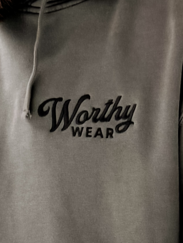 Embroidered Worthy Wear washed hoodie in muted gray with a dark embroidered logo on the chest.