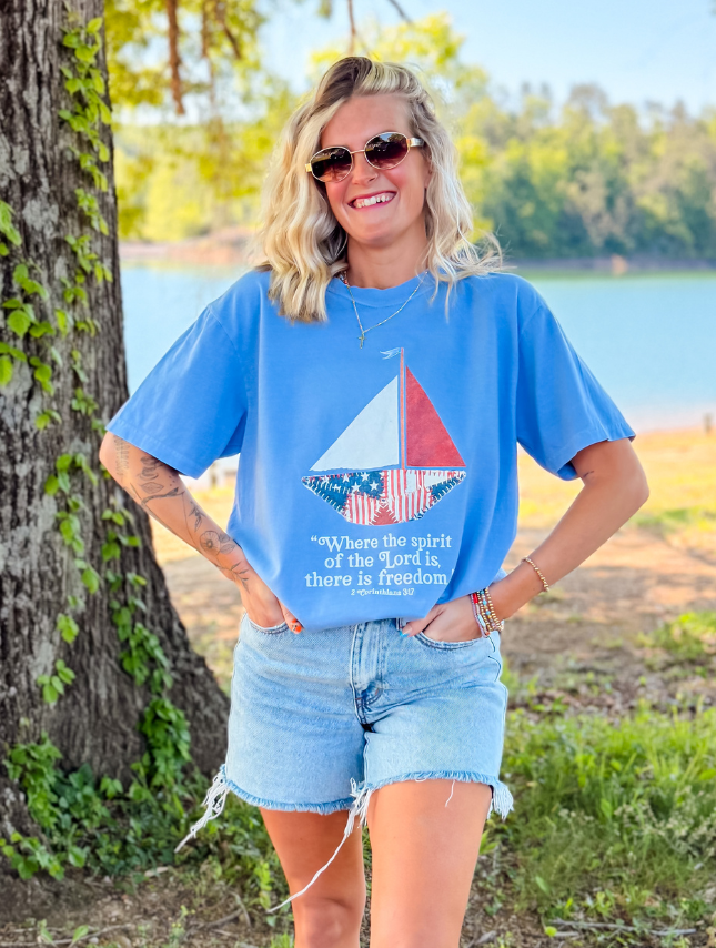 Patchwork sailboat tee in light blue, featuring a colorful sail design and the text "Where the spirit of the Lord is, ther...