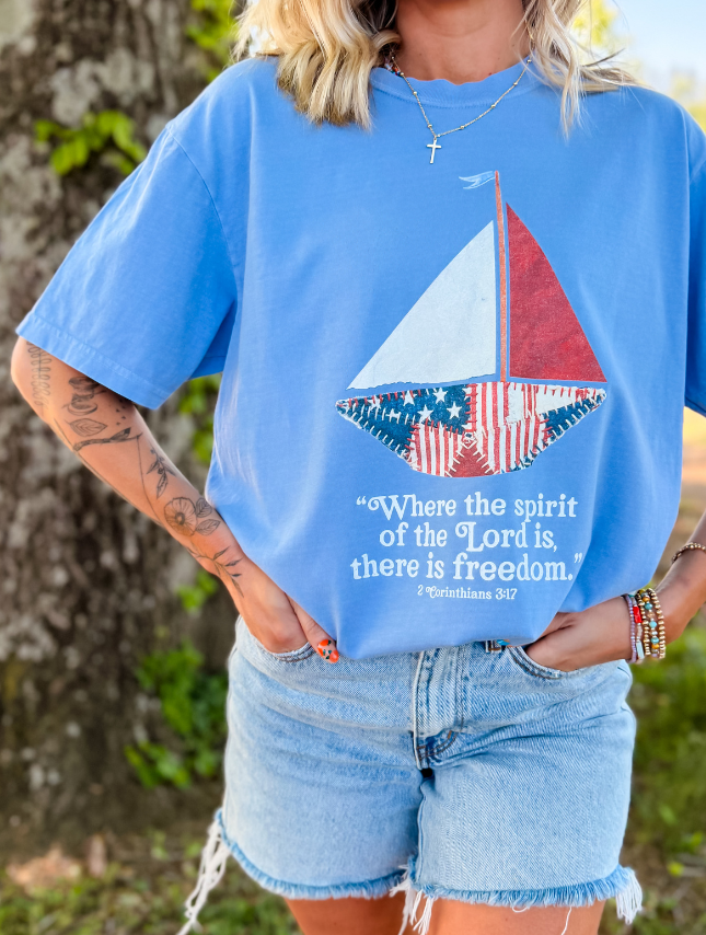 Blue patchwork sailboat tee featuring a red, white, and blue sail with the text "Where the spirit of the Lord is, there is...