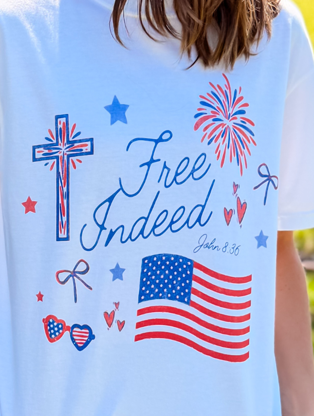 Free Indeed tee featuring a cross, fireworks, stars, and an American flag design in red, white, and blue colors.