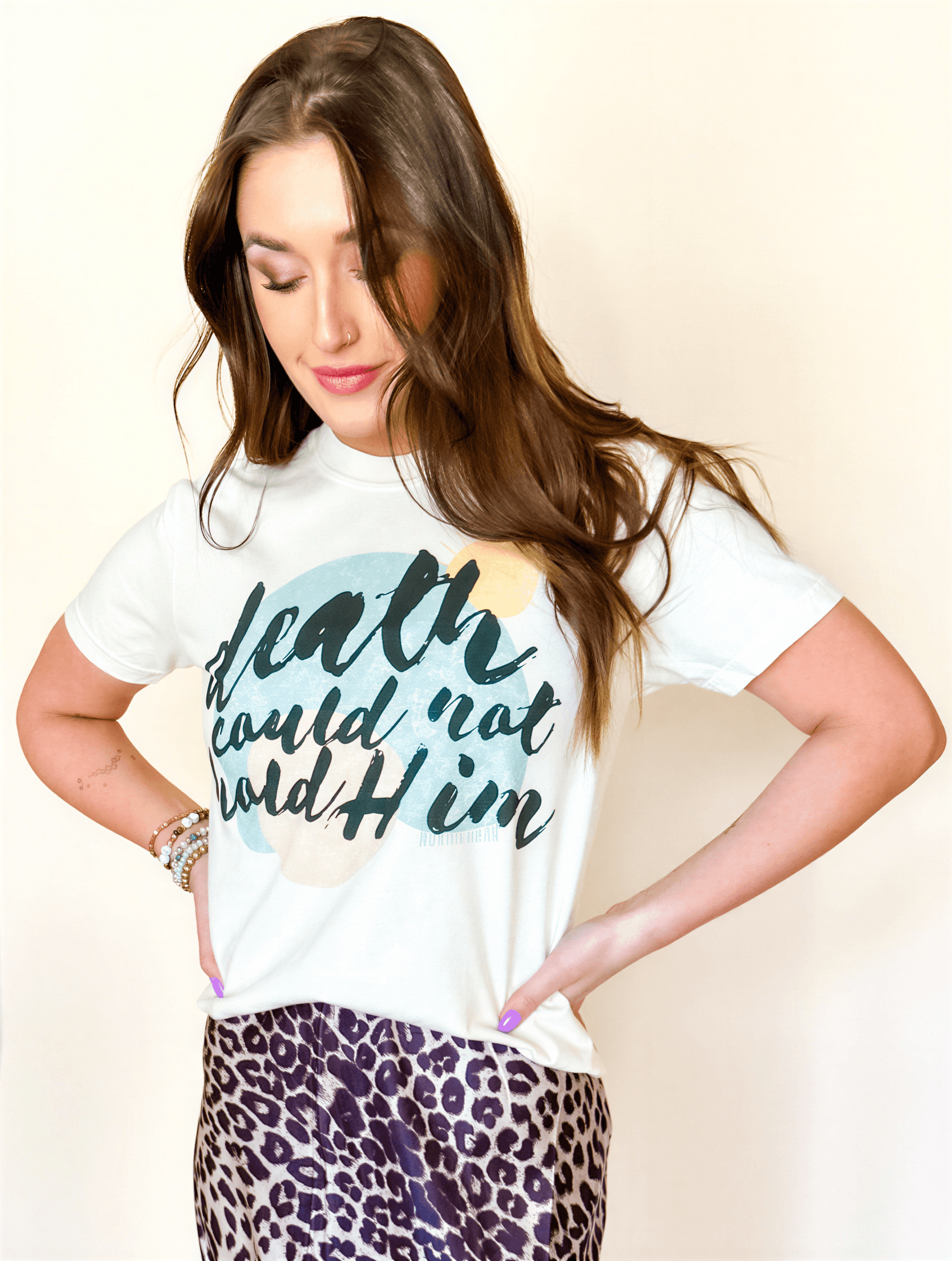 Woman wearing a white t-shirt with text and a leopard print skirt on a plain background