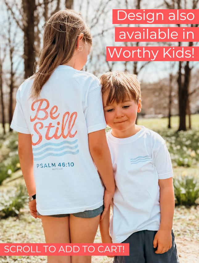 Be Still tee in white worn by a girl and a boy outdoors, featuring text and wave designs on the back.