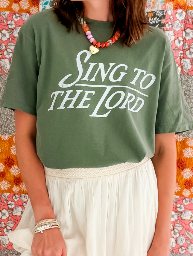 Green "Sing To The Lord" tee worn with a white skirt, accessorized with a colorful beaded necklace.