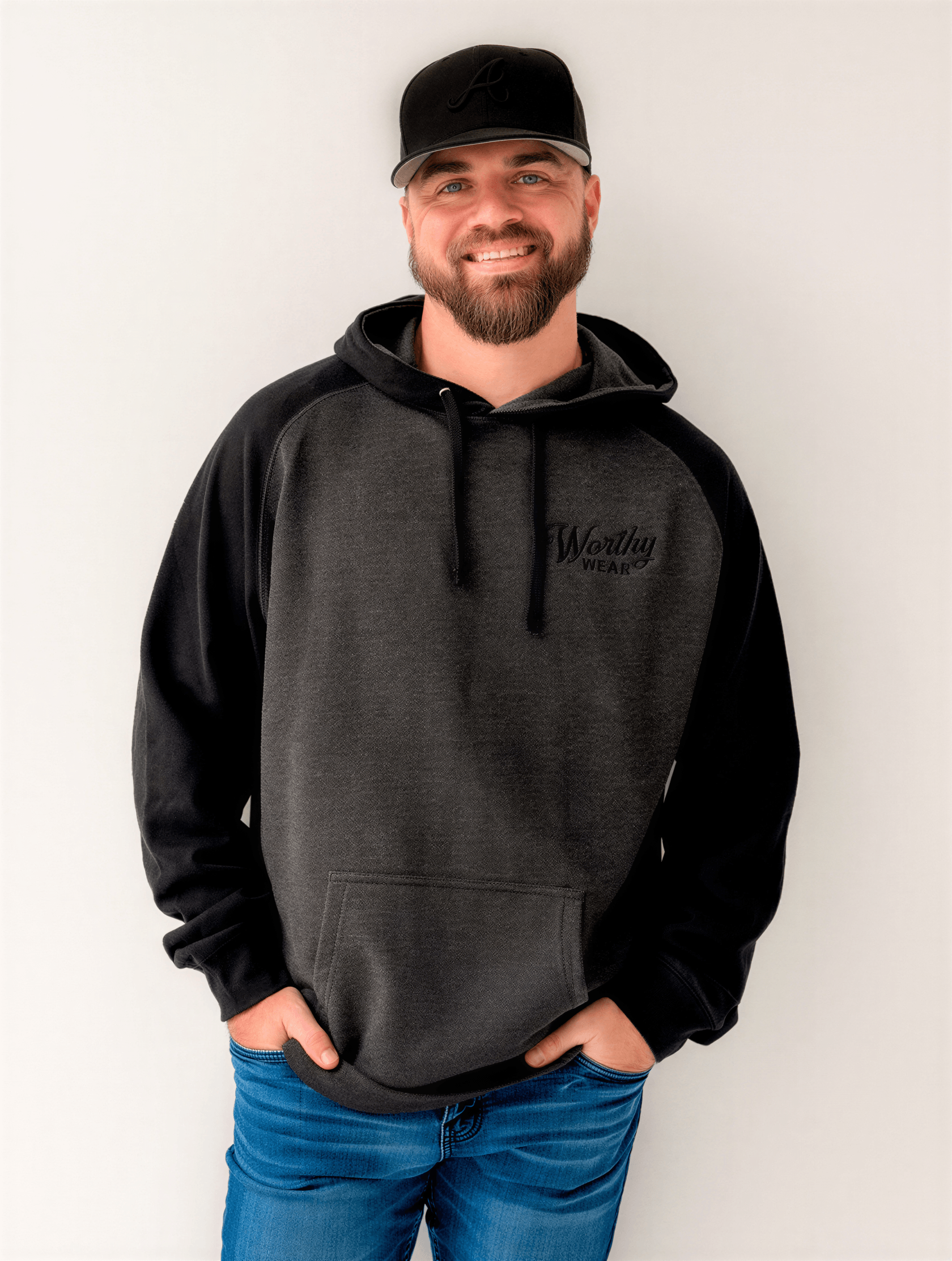 Two-tone embroidered Worthy Wear hoodie in black and gray, worn by a man with a beard, standing against a white background.