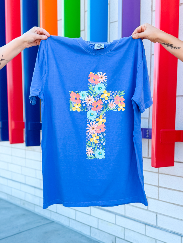 Blue t-shirt with a colorful floral cross design held up against a colorful background.