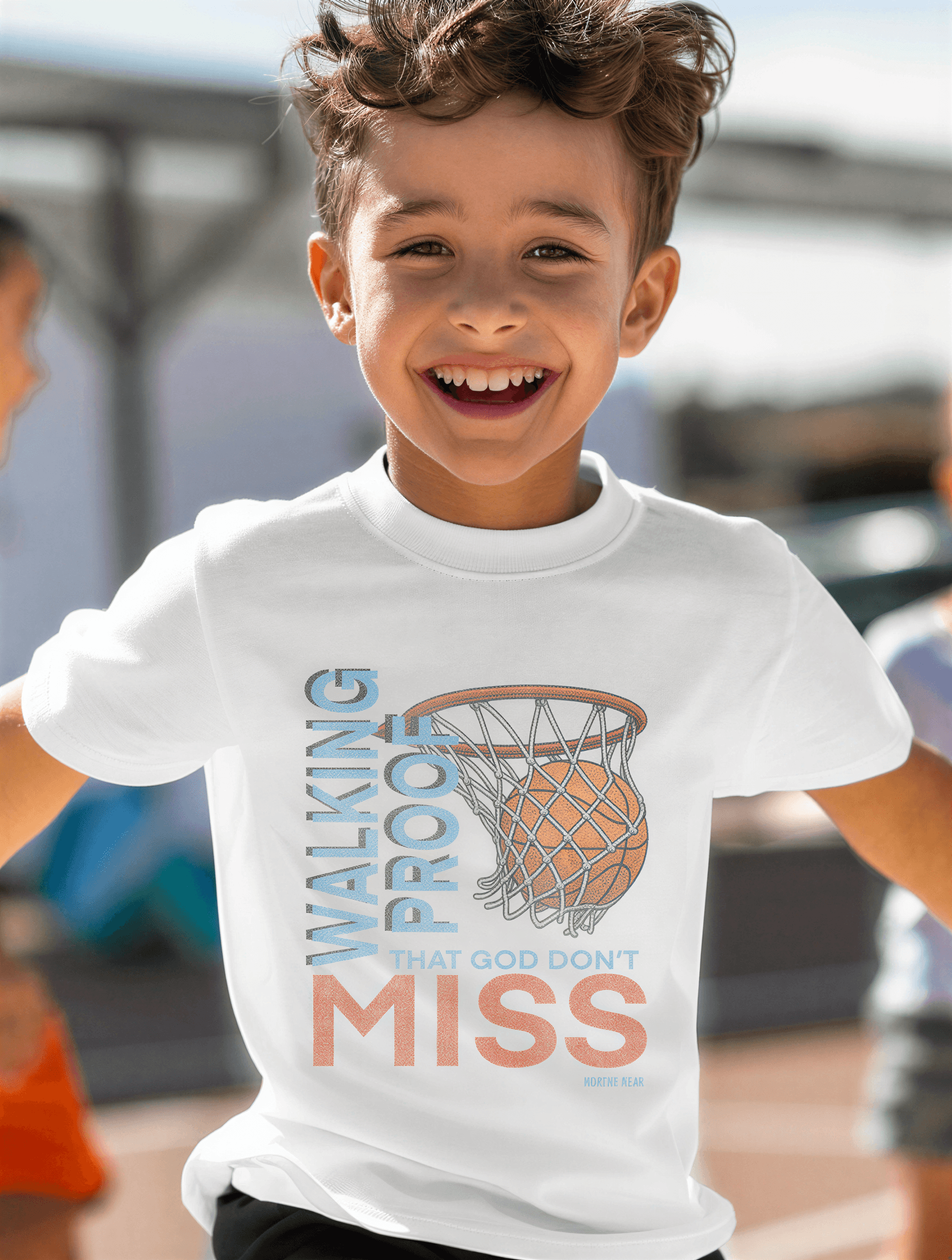 Child wearing a white t-shirt with a basketball graphic and text outdoors.