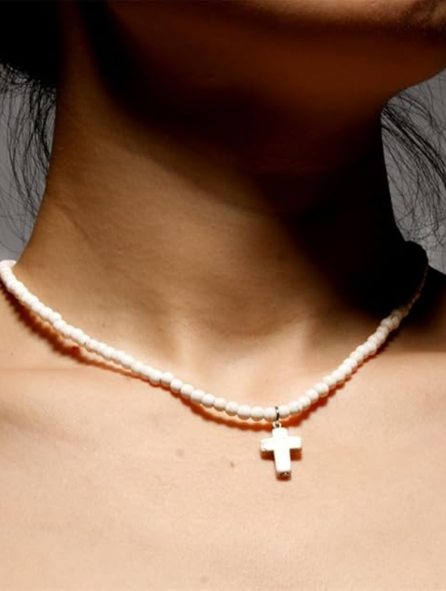 White beaded cross necklace worn around the neck, featuring a small silver cross pendant.
