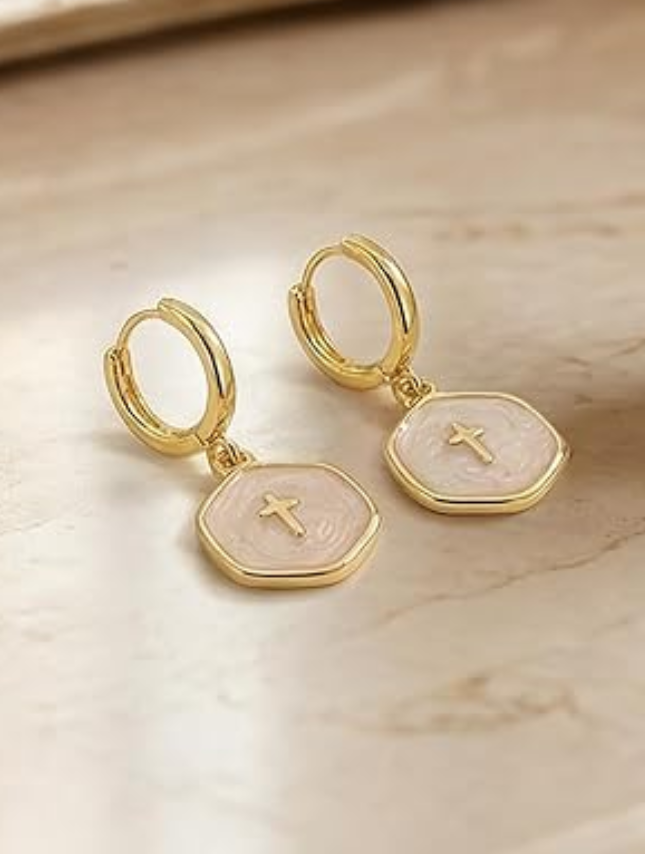 White pearl cross drop earrings with gold accents on a marble surface.