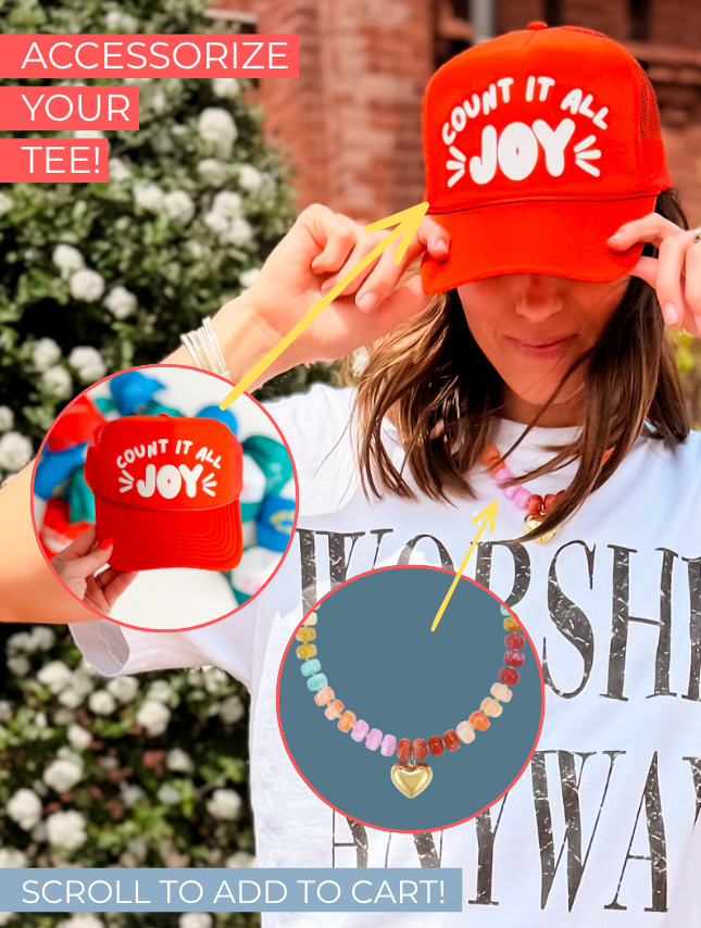Worship Anyway tee in white, featuring bold black text, worn by a person with a colorful necklace and red cap.