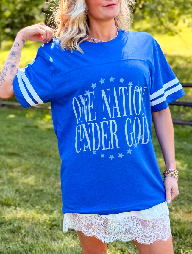 Blue jersey tee featuring "One Nation Under God" text and white striped sleeves, worn by a model outdoors.