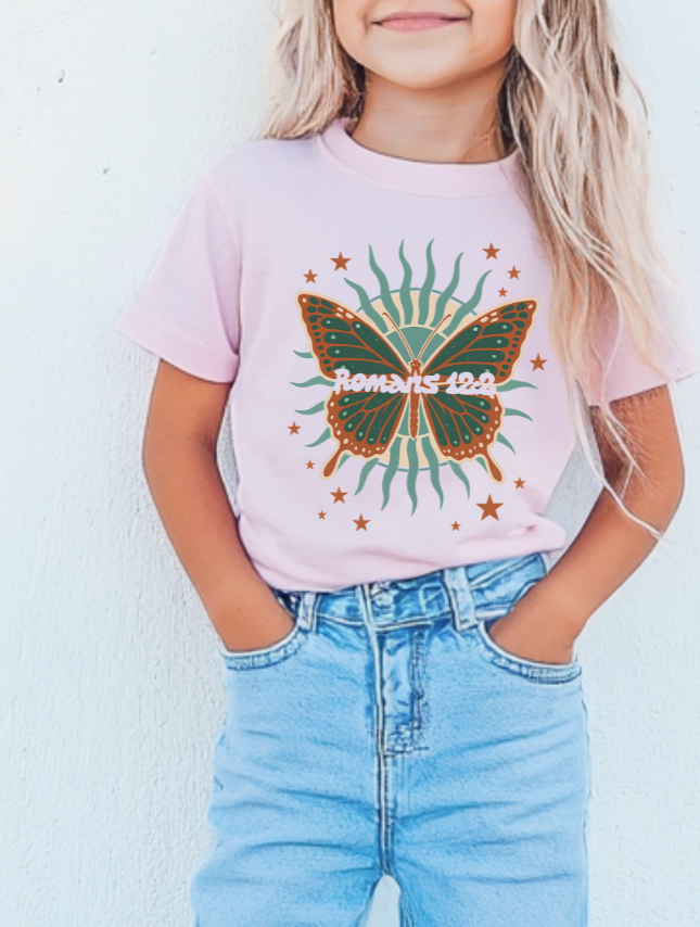 Child wearing a pink t-shirt with a butterfly graphic and text, standing against a light blue background.