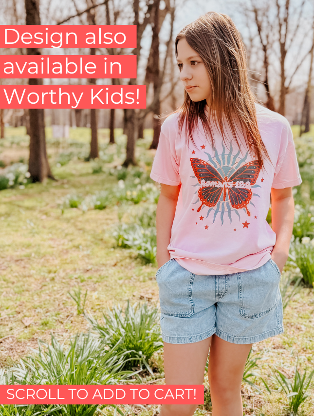 Romans 12:2 tee in pink featuring a butterfly graphic with stars, worn by a girl in a natural outdoor setting.