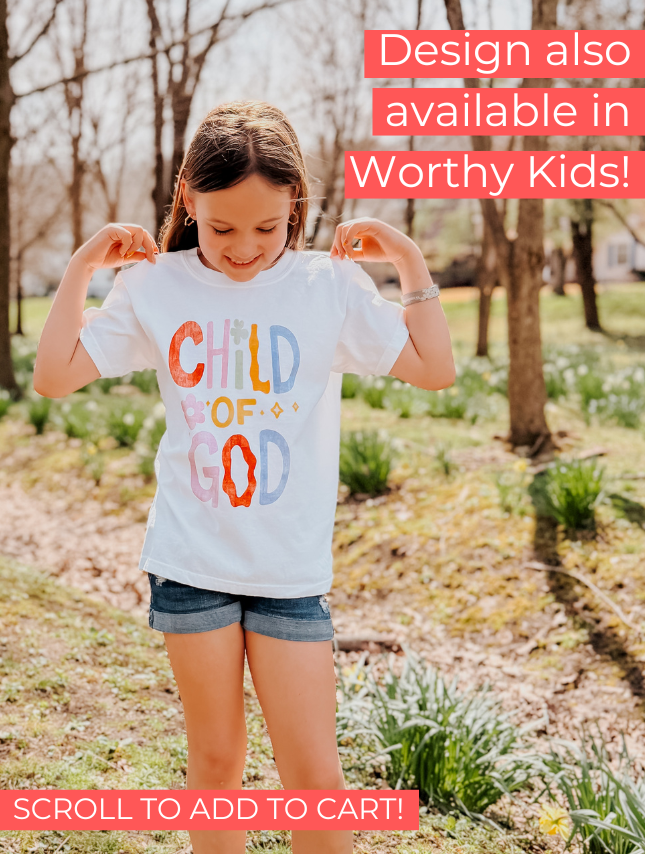 White Child of God tee worn by a girl in a grassy area, featuring colorful text design and casual shorts.