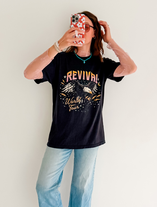Black Revival World Tour tee featuring eagle graphics, worn with light blue jeans and layered with a sheer long-sleeve top.