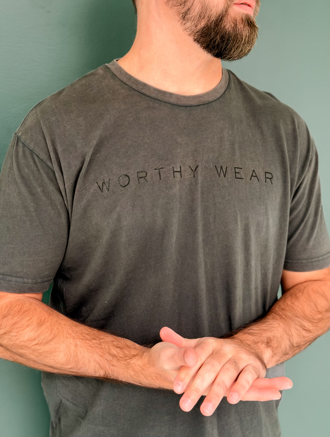 Man wearing a gray 'Worthy Wear' t-shirt against a green background