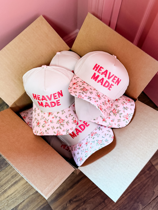 Heaven Made floral hats in a cardboard box, featuring a pink floral brim and white crown with bold text.