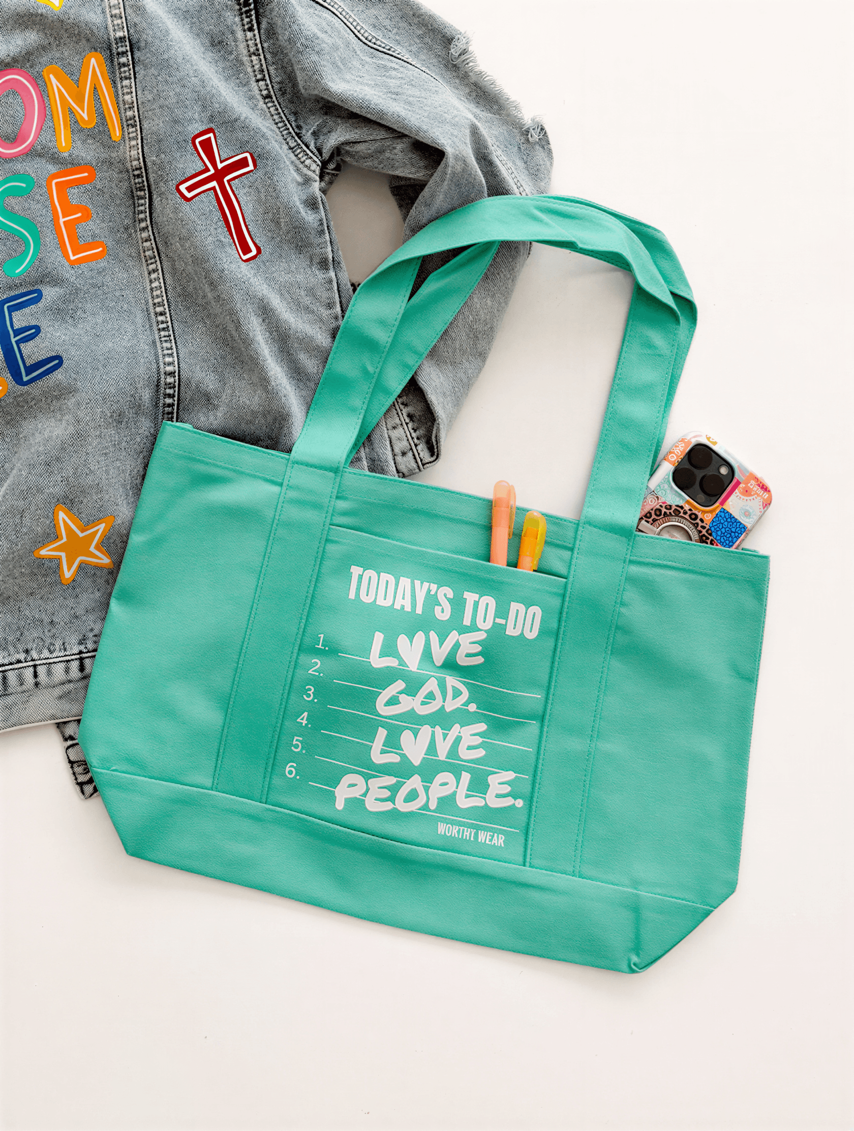 Sea green tote bag with "Today's To-Do" list, colorful markers, and a phone beside a denim jacket with colorful lettering.