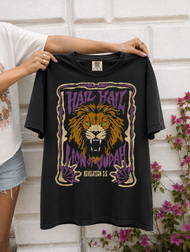 Black t-shirt featuring a lion graphic with "Hail Hail Lion of Judah" text and purple accents, held against a white wall.