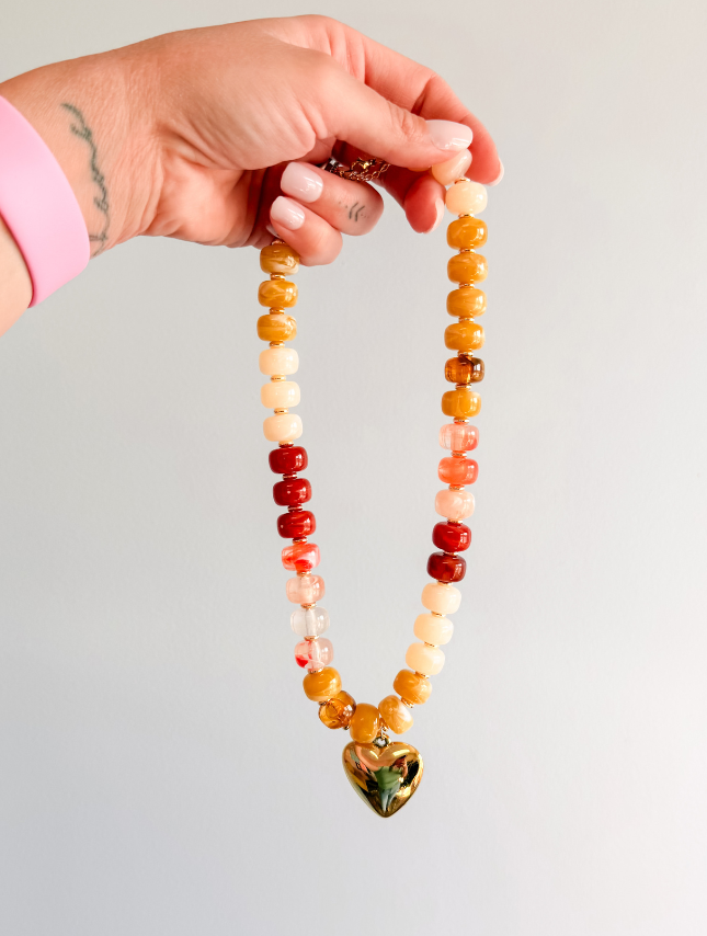 Chunky neutral heart necklace featuring colorful beads in red, yellow, and cream with a gold heart pendant.