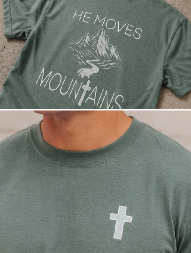 He Moves Mountains tee in moss green featuring mountain and river graphic with a cross on the chest.
